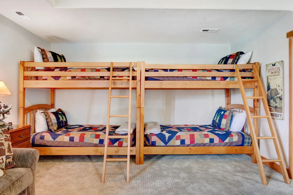 A playful bunkroom with multiple bunk beds adorned in colorful quilts and a wooden ladder. A nightstand with a lamp adds warmth, creating a fun atmosphere perfect for sleepovers and family bonding.