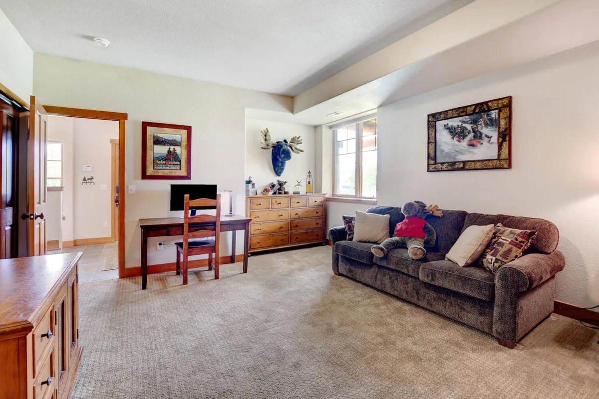 A cozy, comfortable living/dining area featuring a sofa, table, decorative moose head, and a small desk workspace. This space feels homey and practical, with natural light filtering in, perfect for remote work or relaxing after a day out.