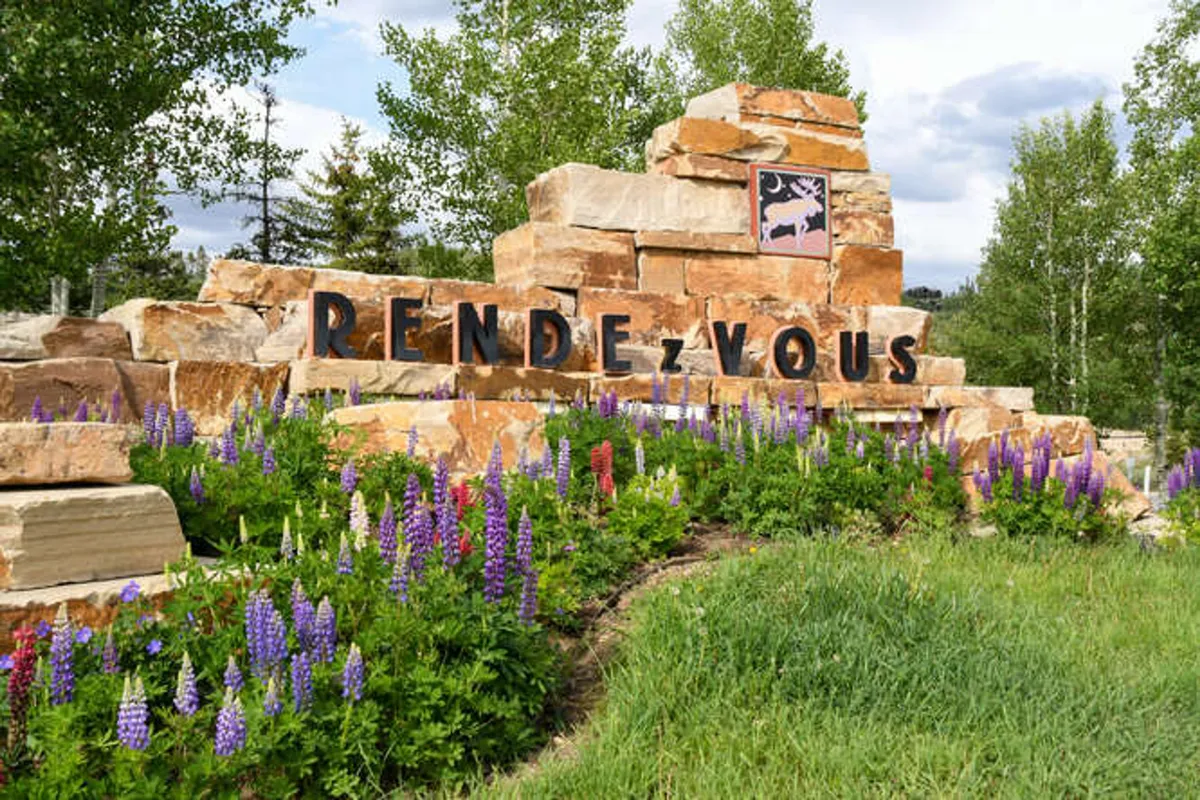 A welcoming stone sign surrounded by colorful flowers and vibrant greenery creates a sense of arrival and community. The natural setting hints at outdoor adventures and the beauty of the surrounding neighborhood.