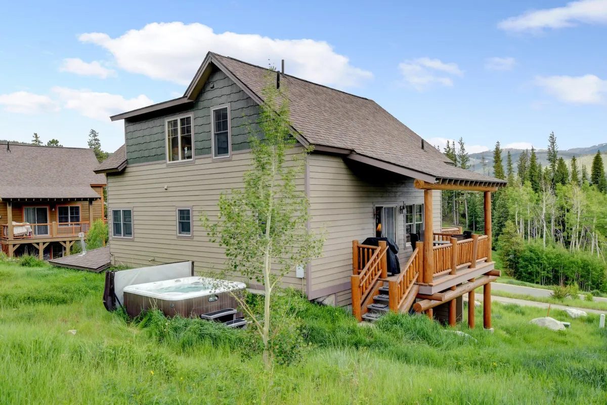 A serene wooden deck with a jacuzzi set amidst lush greenery and a distant mountain backdrop. The space suggests relaxation and rejuvenation after a day of adventure, with the inviting hot tub and scenic views promising a peaceful retreat.