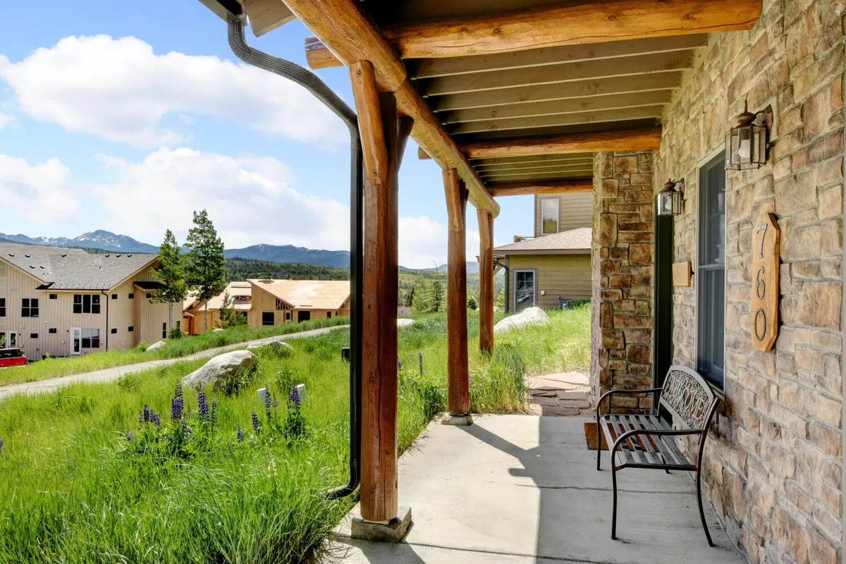 A welcoming wooden porch with stone façade, set against a backdrop of mountains. The area looks ideal for relaxing with a cup of coffee, casual gatherings, or unwinding with a pet after work.