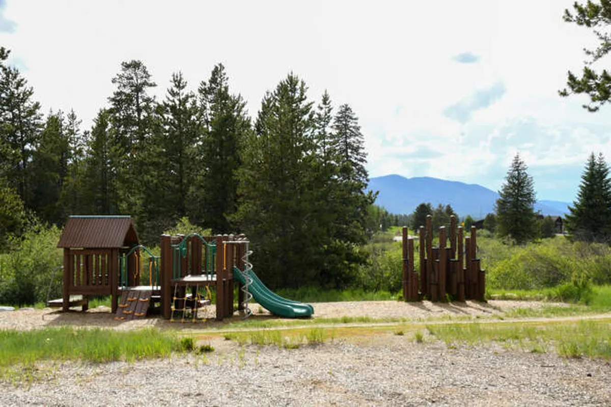 A vibrant playground structure with green slides is nestled among trees, with children actively playing. The scene radiates joy and offers a clear sense of outdoor family recreation and adventure, perfect for younger kids.